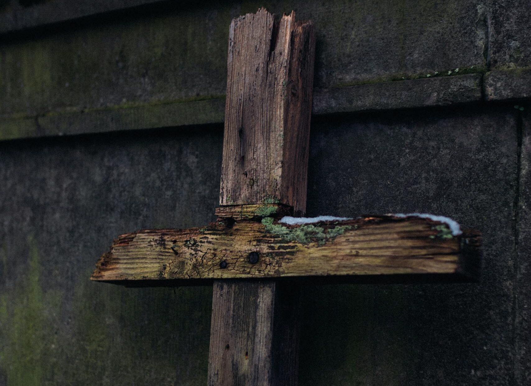 A rustic wooden cross leaning against a concrete wall, symbolizing faith and time.