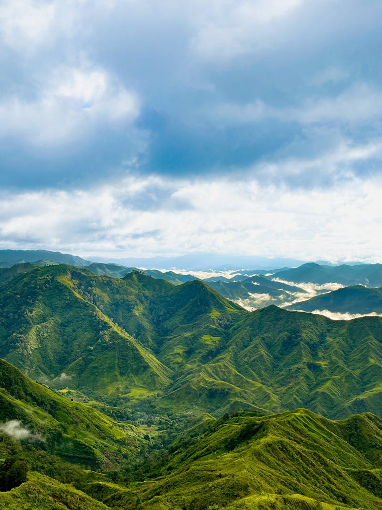 Vast green mountain range with clouds, showcasing nature's beauty under a clear blue sky.